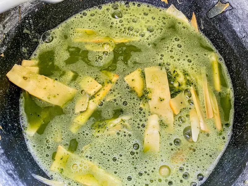 Adding blended yanang and rice mixture to bamboo shoots while cooking soup.