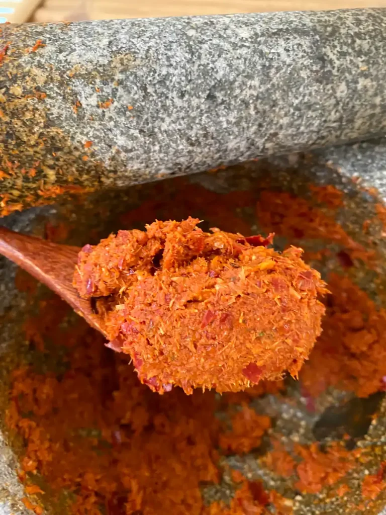 Authentic panang curry paste in a wooden spoon over a granite mortar.