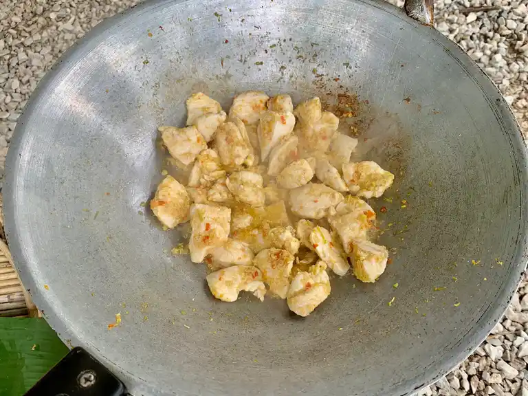 Chicken pieces stir-frying in lemongrass paste inside a hot wok.