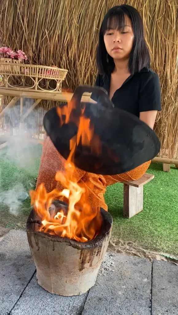 Thai woman stir-frying over an open flame.