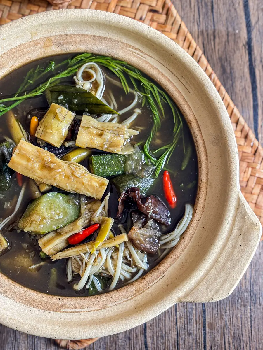 Close-up of Isan-style Thai bamboo soup (gang nor mai) with bamboo shoots, sponge gourd, mushrooms, and dark herbal broth.