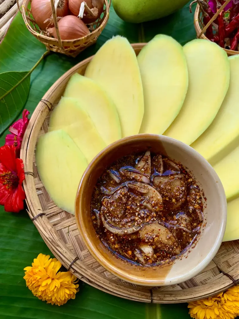 Close-up of Lao fruit dipping sauce with shallots and chili bits, ready to be paired with fresh mango slices.
