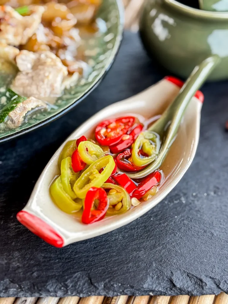 Traditional prik nam som, a Thai chili vinegar sauce served in a ceramic boat dish with sliced red and green chilies.