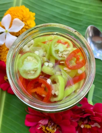Top view of prik nam som, Thai chili vinegar sauce, with red and green chilies on a banana leaf.