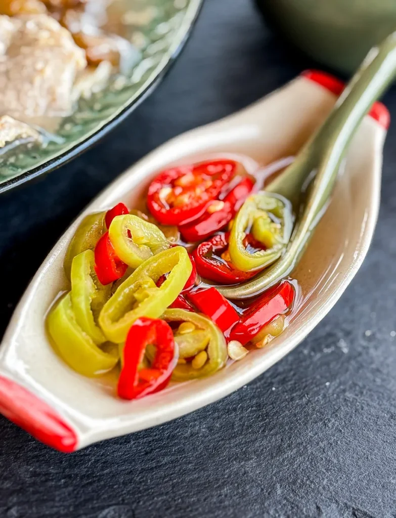 Prik nam som in a small condiment dish, featuring sliced chilies in vinegar with a ceramic spoon.