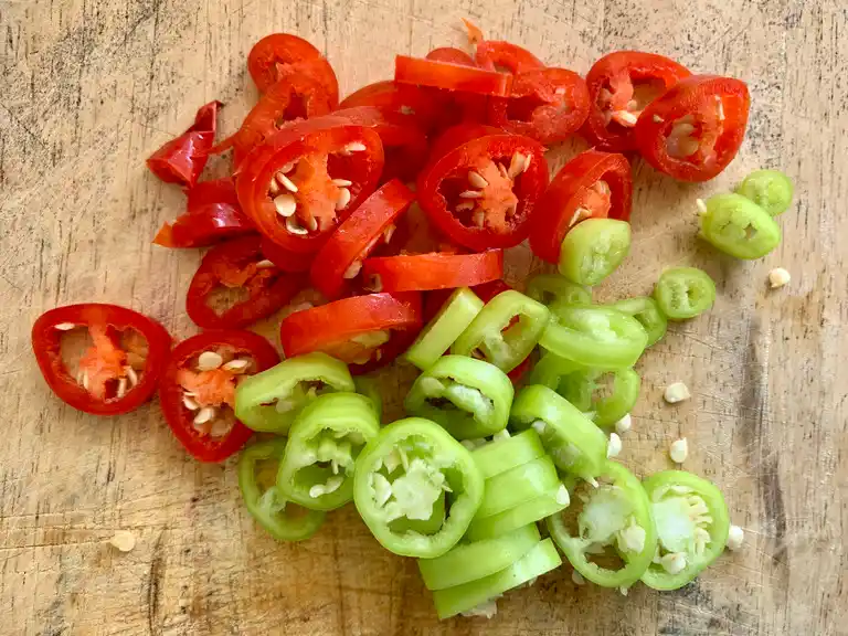 Sliced red and green Thai chilies on a wooden board.