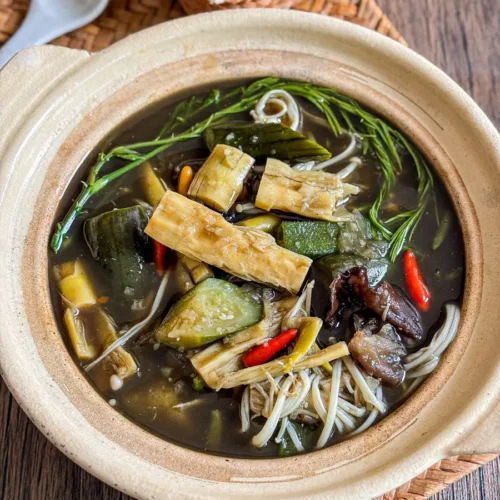 Thai bamboo soup (gang nor mai) with bamboo shoots, enoki mushrooms, chilies, and fresh herbs in a clay pot.