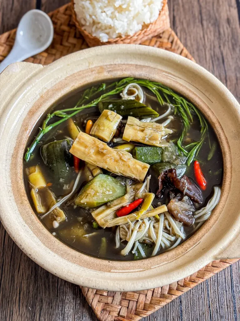 Thai bamboo soup (gang nor mai) with bamboo shoots, enoki mushrooms, chilies, and fresh herbs in a clay pot.