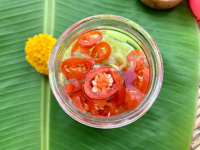 A top-down view of Thai chili vinegar sauce in a glass jar, with sliced red and green chilies floating in vinegar.