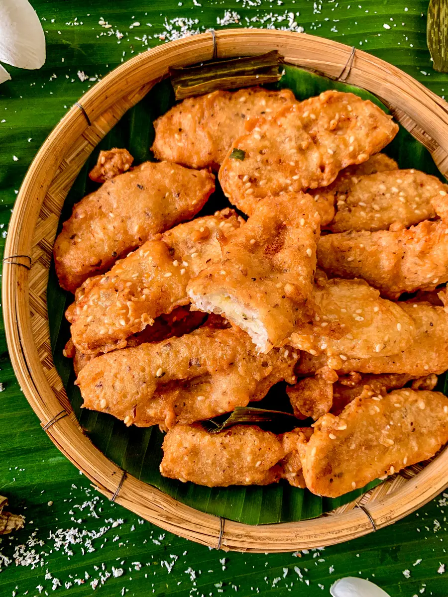 Flat lay of Thai fried bananas with one piece bitten to show the soft inside, served on banana leaves.