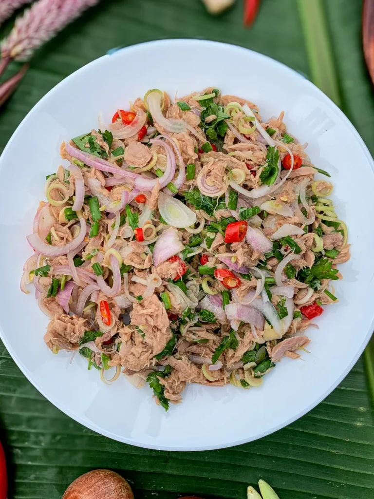 Close-up of Thai tuna salad with lemongrass, red chili, and shallots served on a white plate over banana leaves.