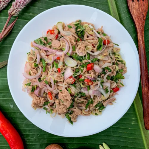 Thai tuna salad made with herbs, shallots, and chili on a white plate surrounded by vegetables.
