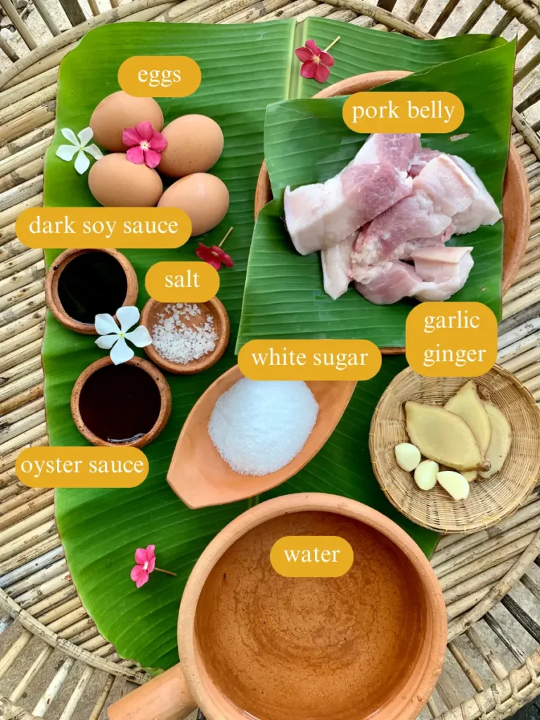 Fresh ingredients for tom khem and their names. Eggs, pork belly, ginger, garlic and seasonings like oyster sauce, dark soy sauce, salt, and white sugar, presented on a banana leaf.