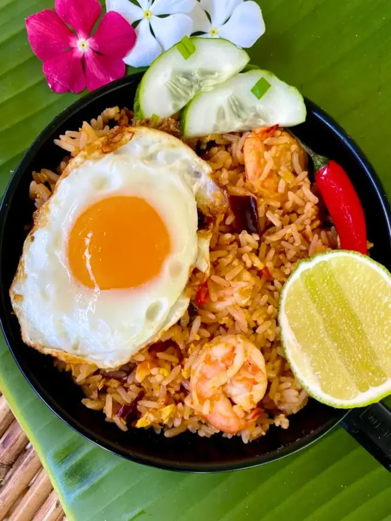 Tom yum fried rice served in a black bowl with a sunny-side-up egg, fresh shrimp, and cucumber slices, garnished with flowers for an easy dinner.