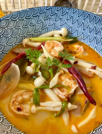 Tom yum kung, a spicy Thai shrimp soup with herbs, spices, and mushrooms in a soup bowl.