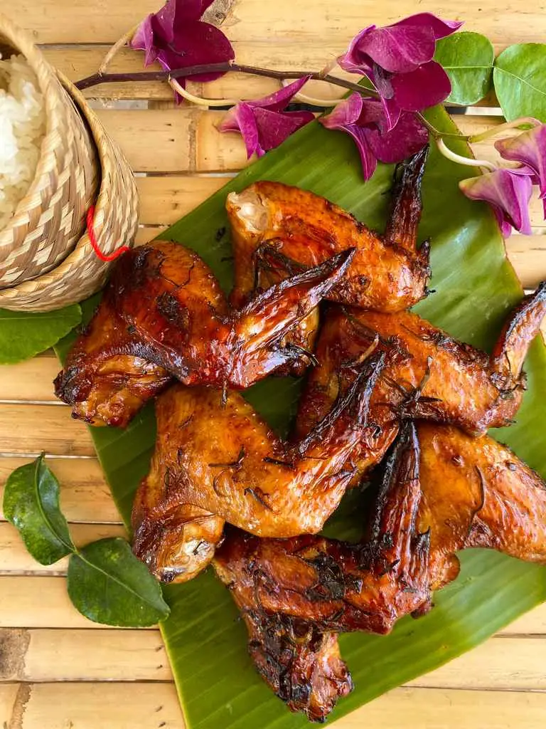 Top-view of Thai chicken wings on a banana leaf, with sticky rice in a traditional basket.