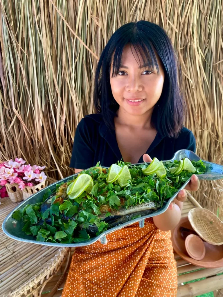 A Thai woman presenting a dish with Thai fish with lime and garlic.