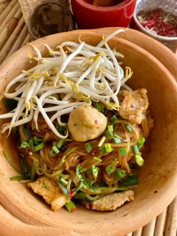 Thai noodle bowl with bean sprouts, meatballs, and green onions in a rustic bowl.