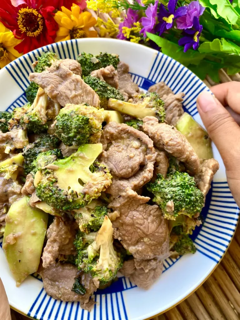 A hand holding a white dish with beef and broccoli stir-fry.