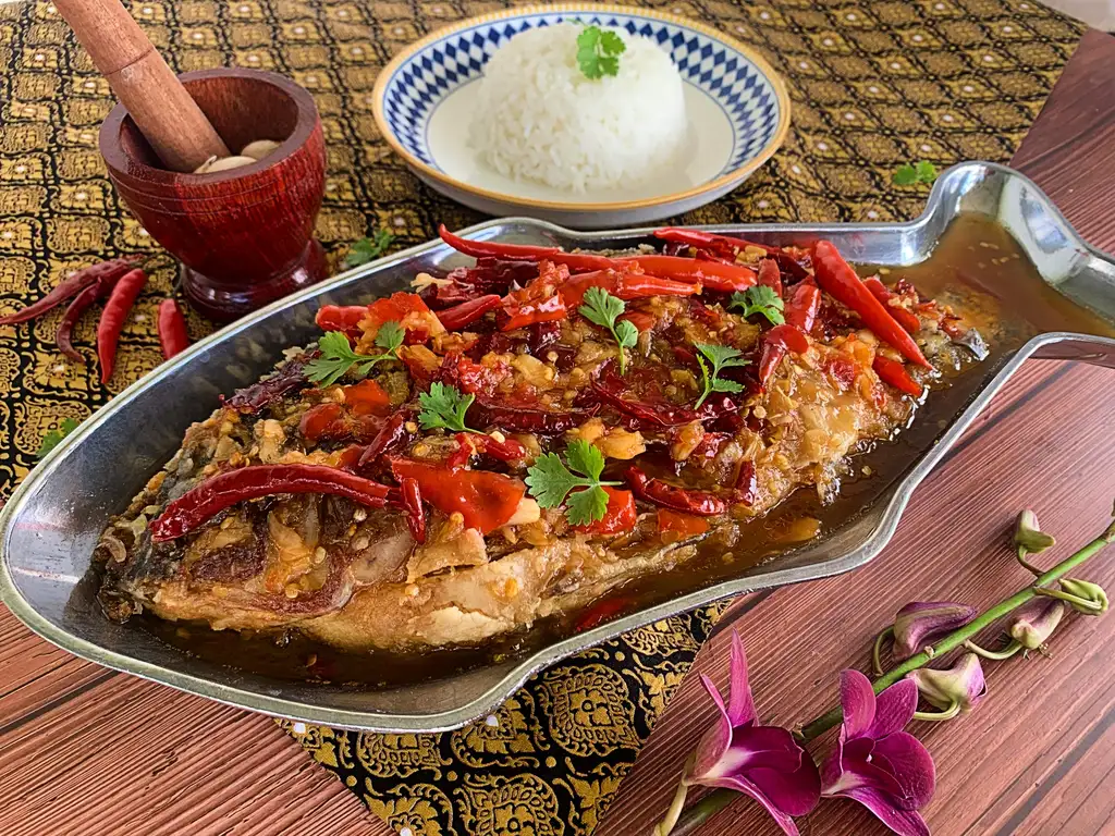 Crispy Thai fish with tamarind sauce in a fish-shaped dish, topped with fresh and dried chilies and cilantro. Served with rice on a separate dish.