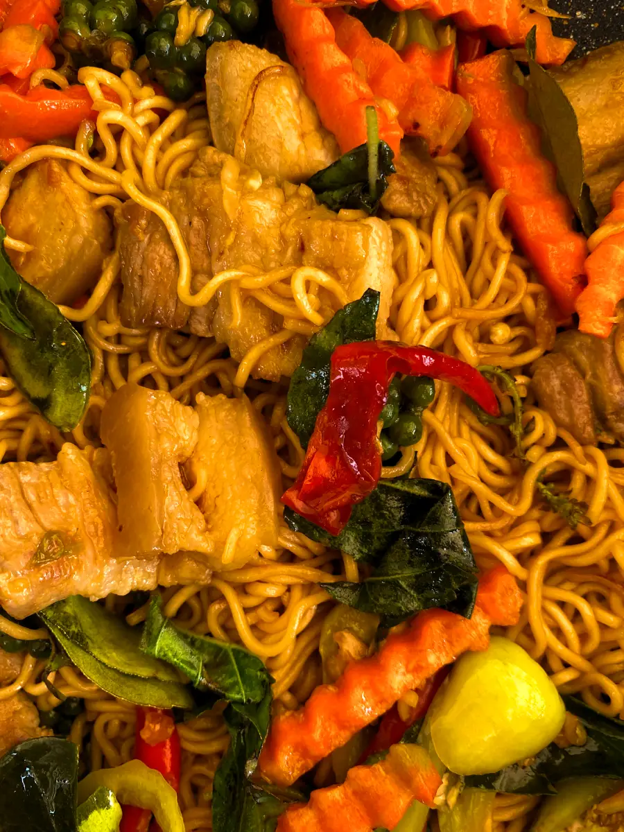 Close-up of stir-fried drunken instant noodles with carrots, chilies, holy basil, and pork.