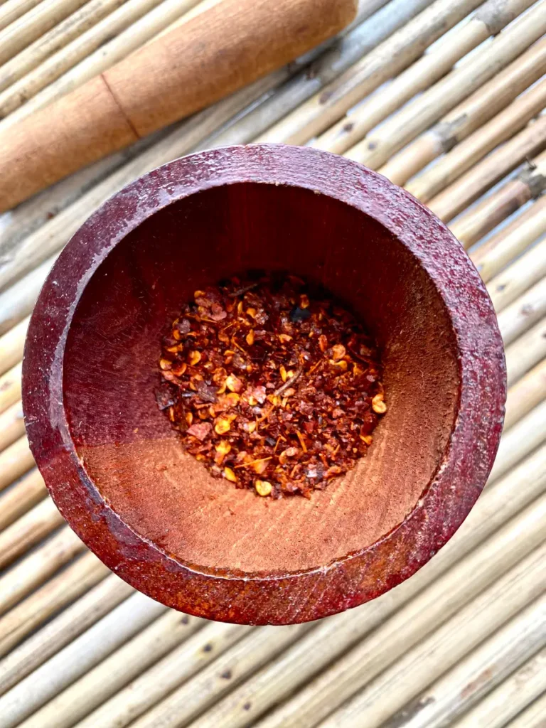 Top-view of red chili flakes in mortar with pestle.