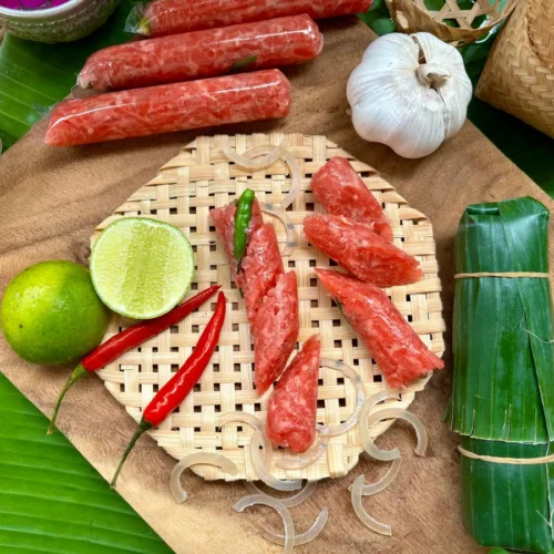 Traditional Lao som moo sausage on a bamboo mat with fresh lime, chili peppers, garlic, and banana leaves.