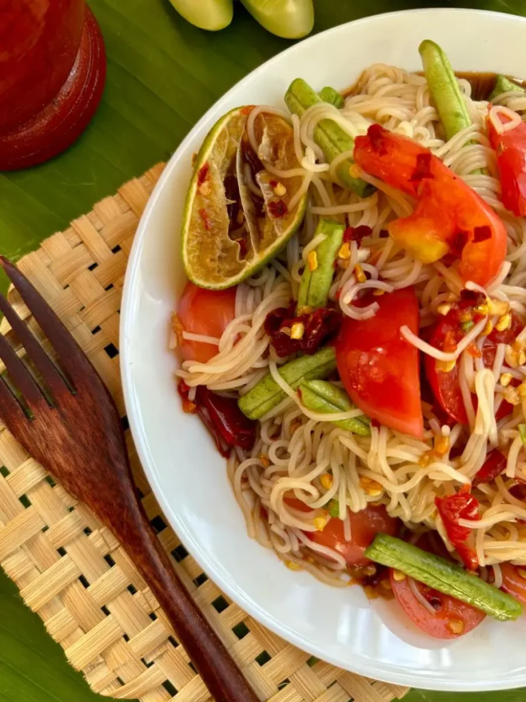 Lao spicy noodle salad with tomato, beans, chili peppers, and lime, served on a white plate.