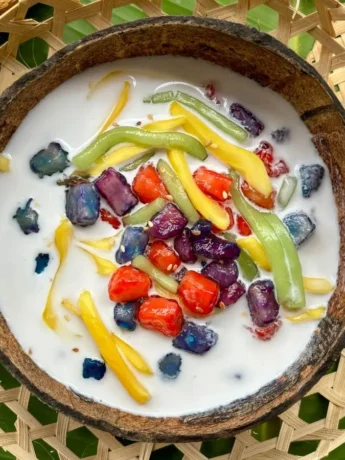 Colorful Thai ruam mit dessert recipe with jackfruit, red rubies, and starchy noodles in creamy coconut milk served in a rustic coconut bowl.