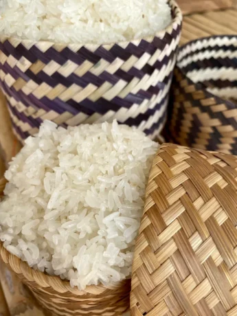 Close-up of freshly steamed Thai sticky rice in a traditional woven bamboo basket.