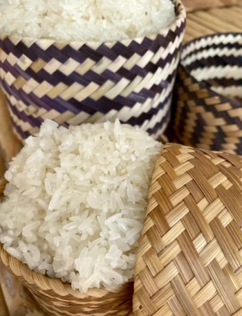 Close-up of freshly steamed Thai sticky rice in a traditional woven bamboo basket.