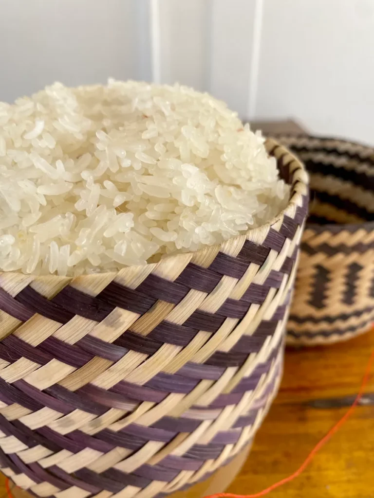 A close-up view of Thai sticky rice in a traditional patterned bamboo basket, highlighting the texture and quality of the rice.