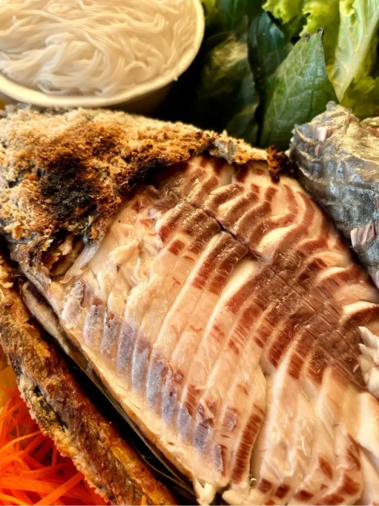 Close-up of pla pao, authentic Thai grilled fish, highlighting the tender, flaky flesh beneath the golden-brown skin.