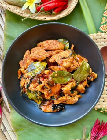 Chicken pad ped, a spicy Thai red curry stir-fry with chicken, with red chilies and kaffir lime leaves presented on a banana leaf.