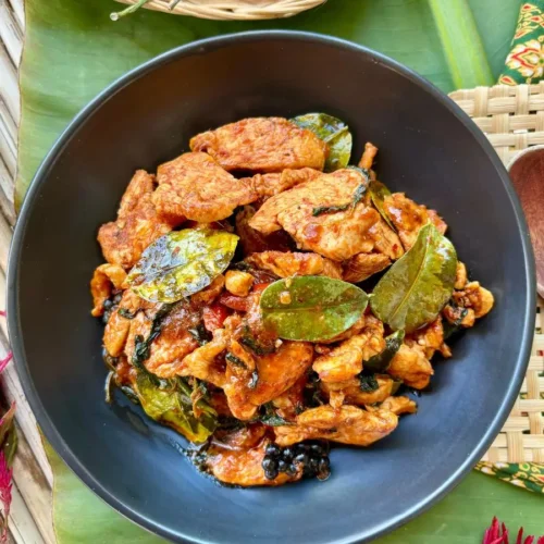 Chicken pad ped, a spicy Thai red curry stir-fry with chicken, with red chilies and kaffir lime leaves presented on a banana leaf.