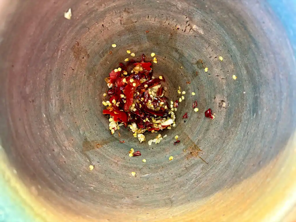 Spices including garlic and dried chilies at the bottom of a mortar, ready to be pounded for thum khao poon dressing.