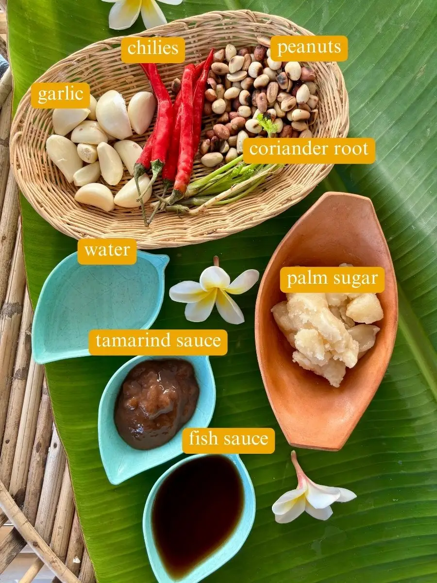 Thai dipping sauce ingredients: fiery red chilies, garlic cloves, peanuts, accompanied by coriander roots, palm sugar, tamarind sauce, and fish sauce.