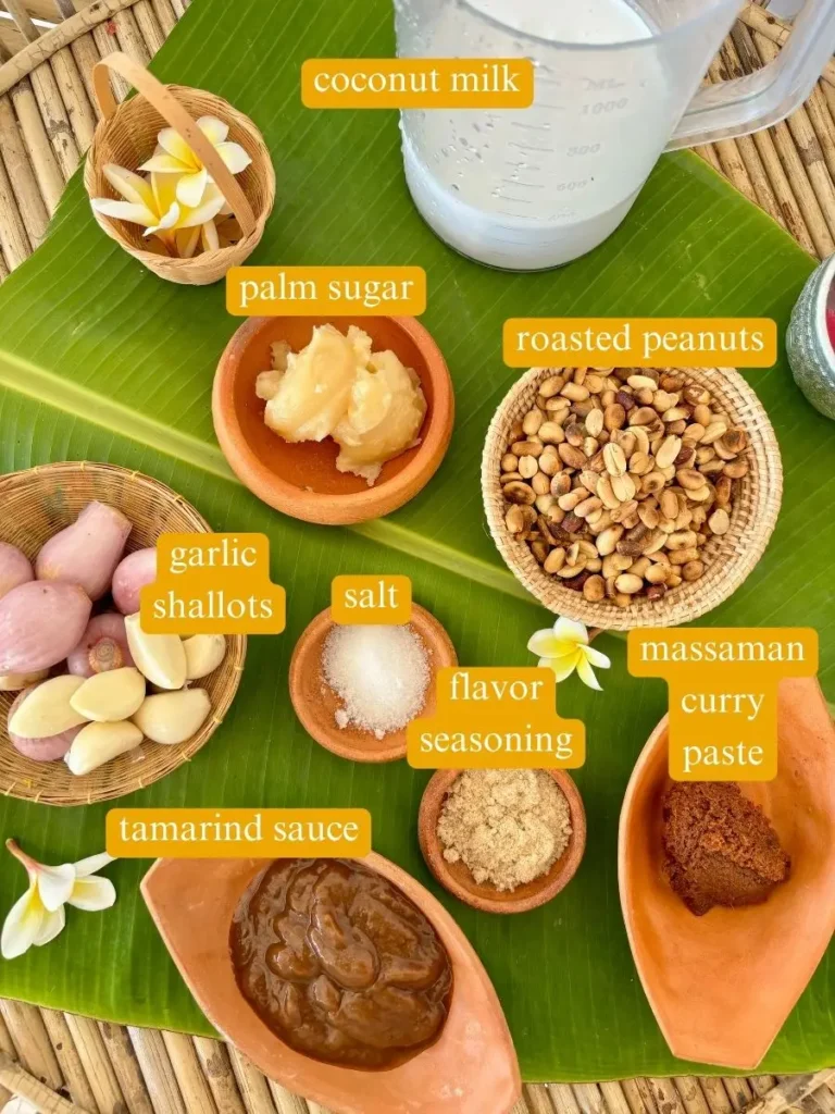 Ingredients for Thai peanut sauce displayed on a banana leaf, showcasing coconut milk, palm sugar, garlic, shallots, roasted peanuts, tamarind sauce, and massaman curry paste.