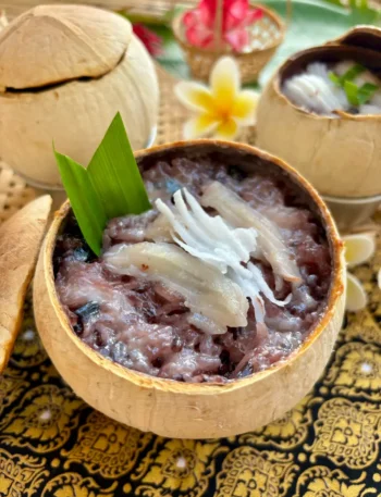 Khao lam, Thai sticky rice in bamboo dessert, with black beans topped with young coconut meat presented in a coconut shell.