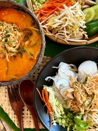 Khao poon, Lao chicken coconut noodle soup, served with fresh bean sprouts, carrots, cucumber, and cabbage, alongside a bowl of spicy red curry soup broth and rice vermicelli noodles.