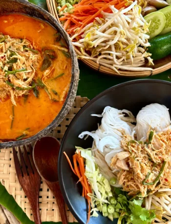 Khao poon, Lao chicken coconut noodle soup, served with fresh bean sprouts, carrots, cucumber, and cabbage, alongside a bowl of spicy red curry soup broth and rice vermicelli noodles.