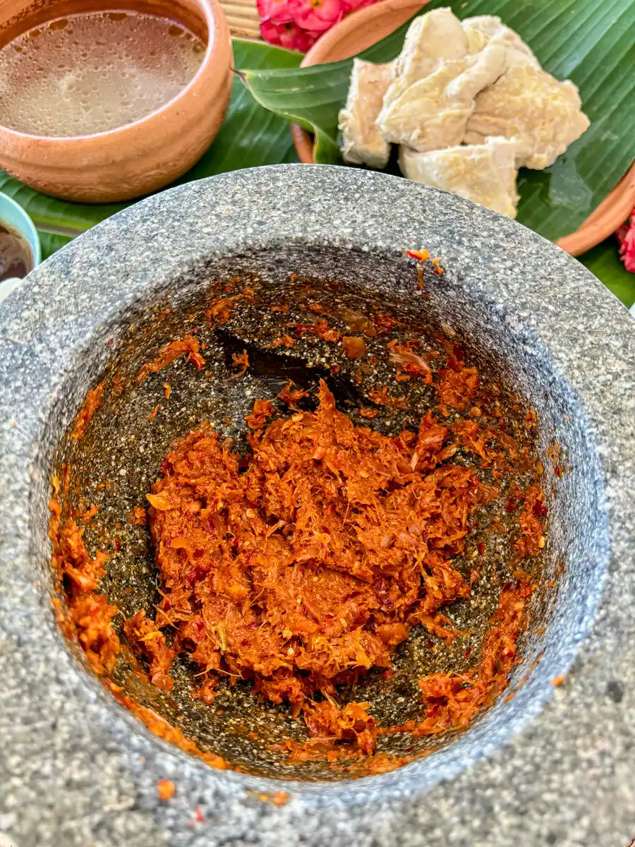 Freshly pounded khao poon curry paste in a stone mortar, surrounded by traditional ingredients.