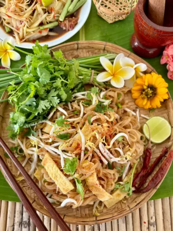 Kua mee on a bamboo plate, a Lao noodle dish with rice noodles, egg, bean sprouts, a sprinkle of chili, garnished with coriander and green onions for an easy Thai recipe.