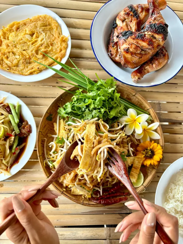 Top-down view of Lao meals with kua mee noodles surrounded by an omelette, grilled chicken, and a side of sticky rice.