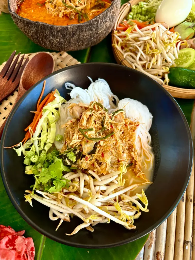 Bowl of Lao noodle soup with chicken, khao poon, ready to serve with rice vermicelli noodles and vegetables, garnished with green onions.