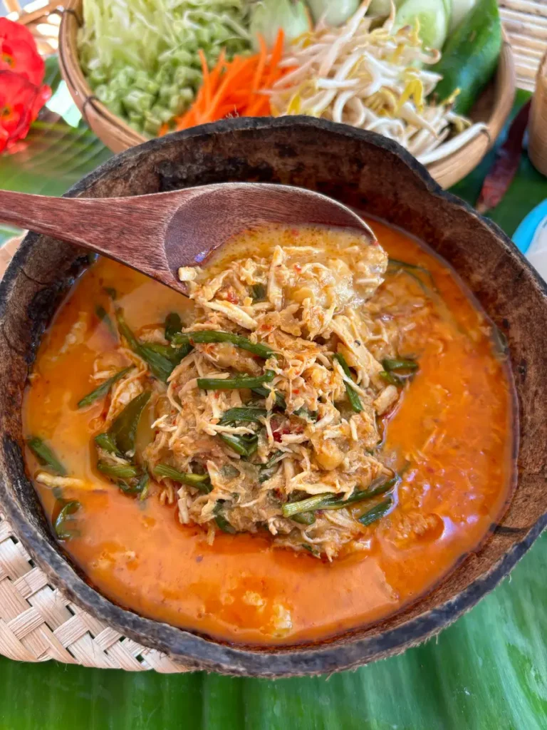 Close-up of spicy Lao chicken coconut noodle soup with shredded chicken and green onions in a rich, red curry coconut broth.