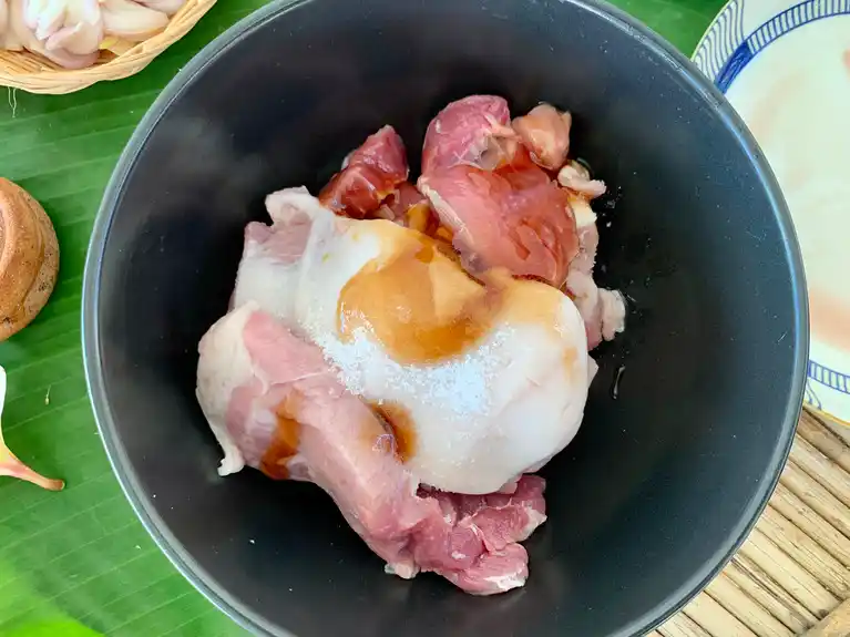 Raw pork shoulder marinating with oyster sauce and sugar in a black bowl.