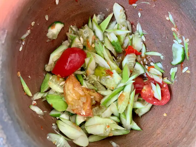 All ingredients, including cucumber, tomatoes, chilies, and lime, gently mixed in a mortar to finish thum mak thang.