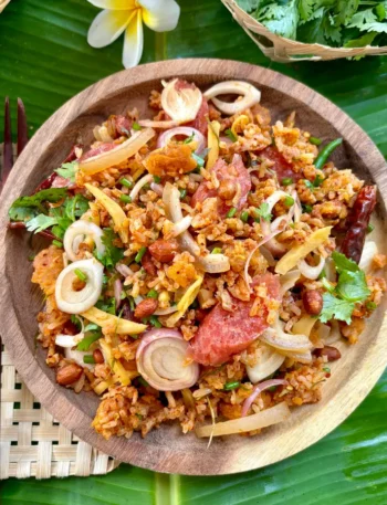 Nam khao tod Thai crispy rice salad with fresh herbs and sour sausage on a wooden plate over banana leaf.