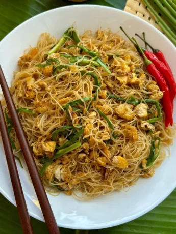 A plate of pad mee garnished with green onions and red chilies, ready to be eaten with wooden chopsticks.